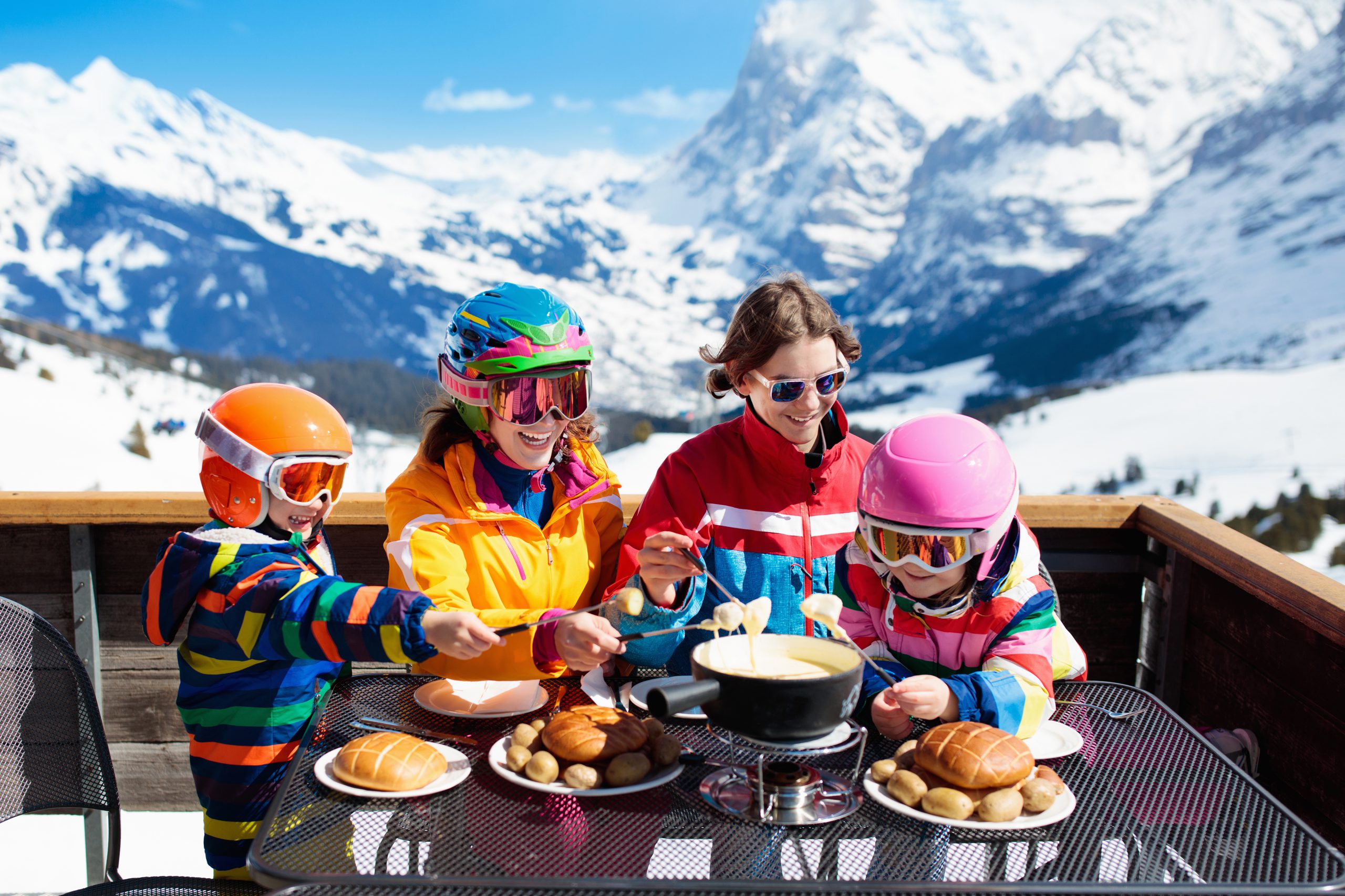 Family with children enjoying apres ski lunch with traditional Swiss raclette and cheese fondue in restaurant on top of snow covered mountain on winter or Christmas vacation. Parents and kids skiing.