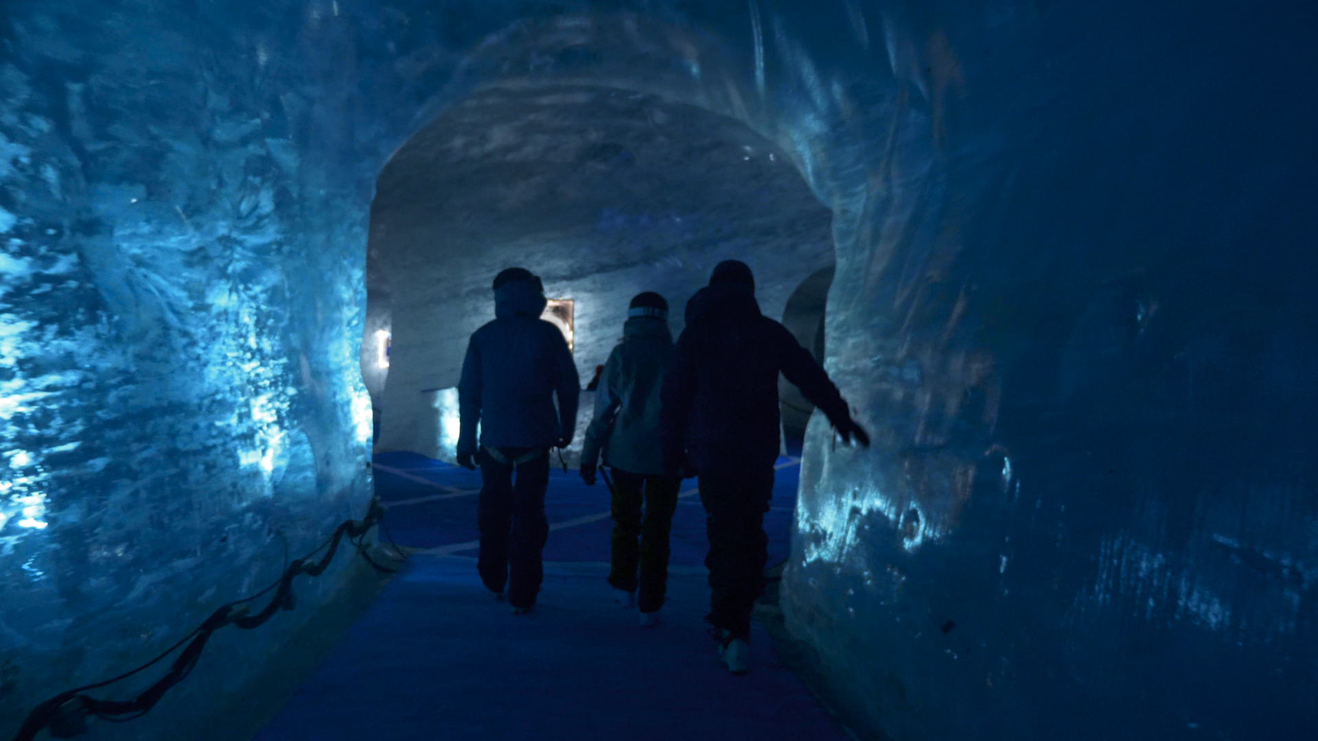 Three skiers walk through a cave of blue ice on their way back from the Vallee Blanche