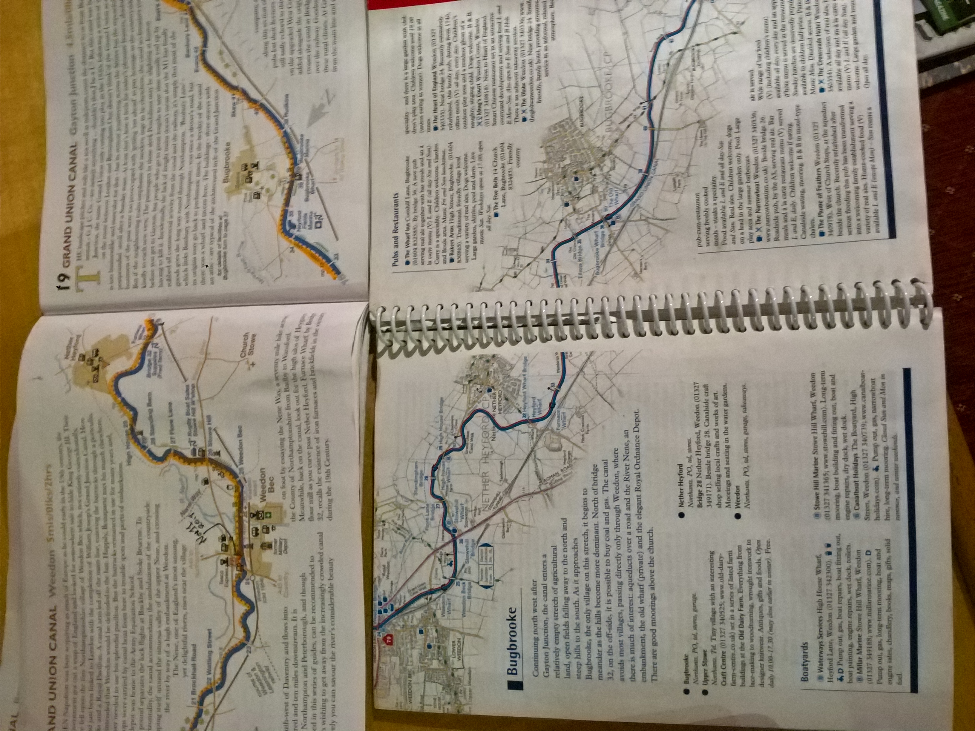 Photo of two open guidebooks with maps of the Grand Union Canal in Northamptonshire. The maps only include half a mile or a mile on either side of the canal, so they are very long and stretched out, cutting across the pages. The descriptive text wraps around the shape of the map.