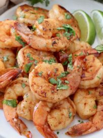 cooked shrimp piled up on plate with lime wedges