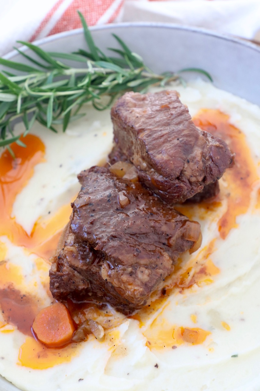 braised short ribs on top of mashed potatoes in bowl