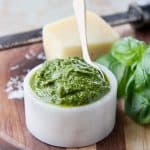 Basil pesto in white marble bowl with small gold spoon in the bowl