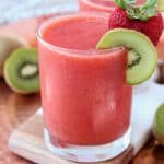 Strawberry slush in glass with kiwi slice and strawberry on the rim of the glass