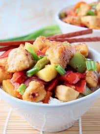 Sweet and sour chicken with bell peppers and pineapple chunks in bowl with chopsticks