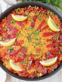 Overhead image of spanish paella in skillet with lemon wedges on top