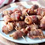 Bacon wrapped dates skewered with toothpicks on white plate
