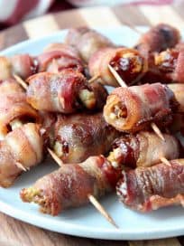 Bacon wrapped dates skewered with toothpicks on white plate