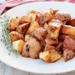 Crispy baked Cajun red potatoes on white plate with fresh thyme sprigs