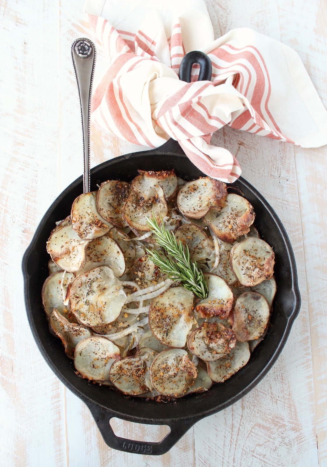 A cast iron skillet on a wooden surface filled with sliced and seasoned potatoes.