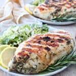 grilled chicken breast on plate with rosemary sprigs and lemon wedges