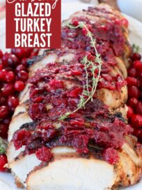sliced turkey breast on plate covered with cranberry sauce and thyme sprigs