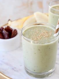 Banana protein shakes in glasses with gold and white striped straw and a small bowl of dates in the background