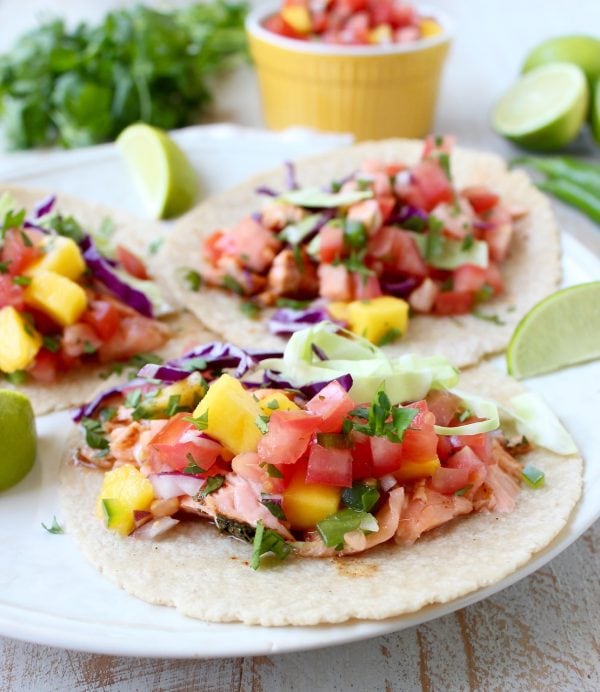 Corn tortillas topped with salmon and mango salsa on a white plate. 