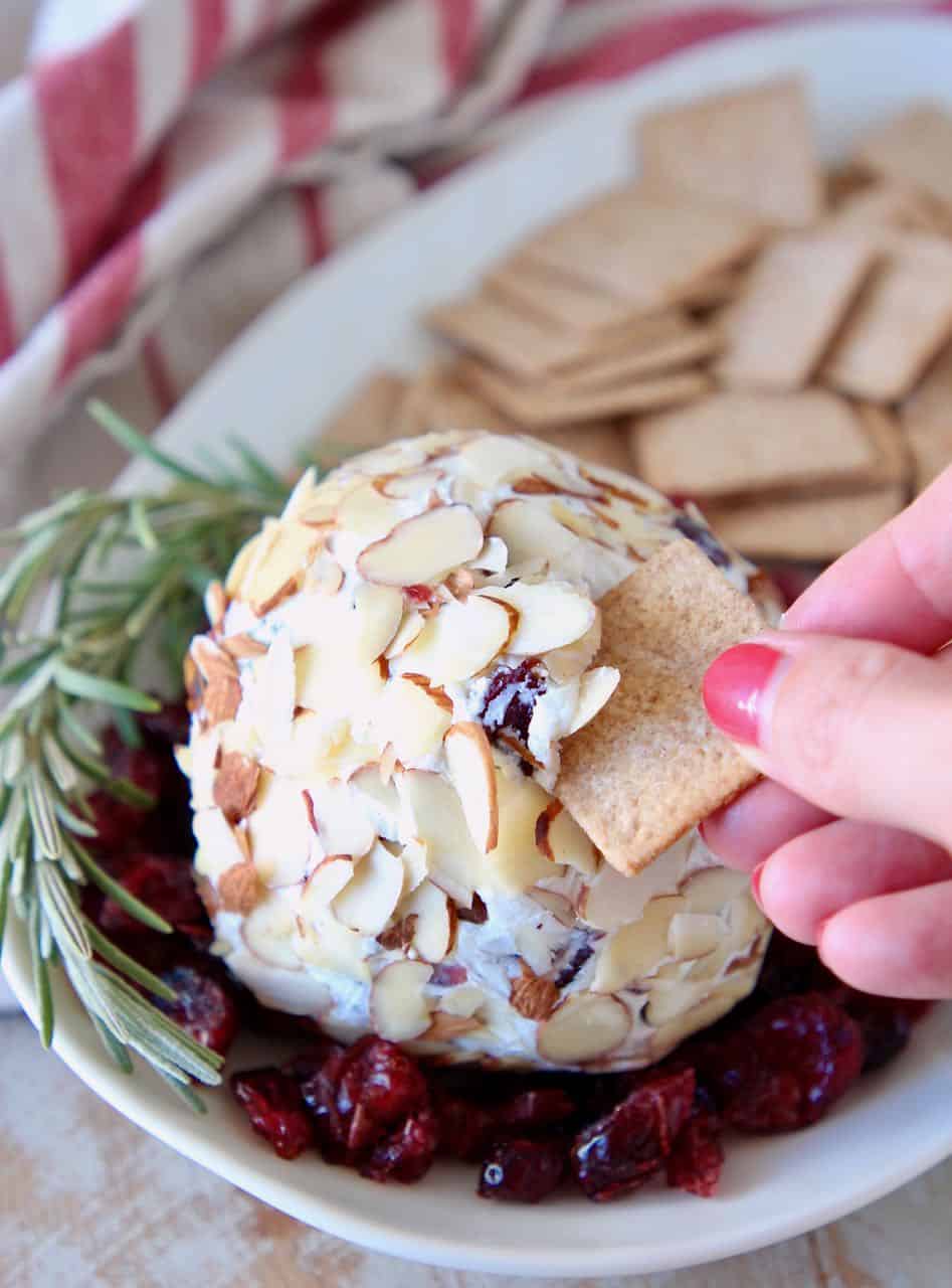 Hand dipping cracker into cheese ball on plate