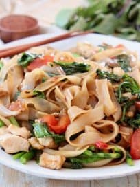 Drunken noodles with tomatoes and Chinese broccoli on white plate with chopsticks on the side