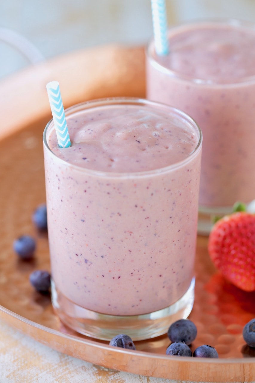 Fruit smoothie in glass with straw on copper tray with fresh strawberries and blueberries