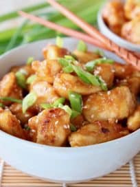 Orange chicken in bowl with scallions and wood chopsticks