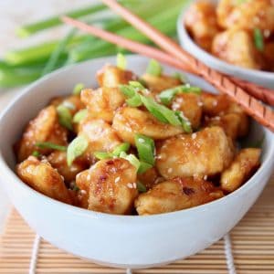Orange chicken in bowl with scallions and wood chopsticks