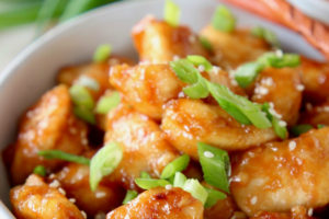 Orange chicken in bowl with diced scallions and wood chopsticks