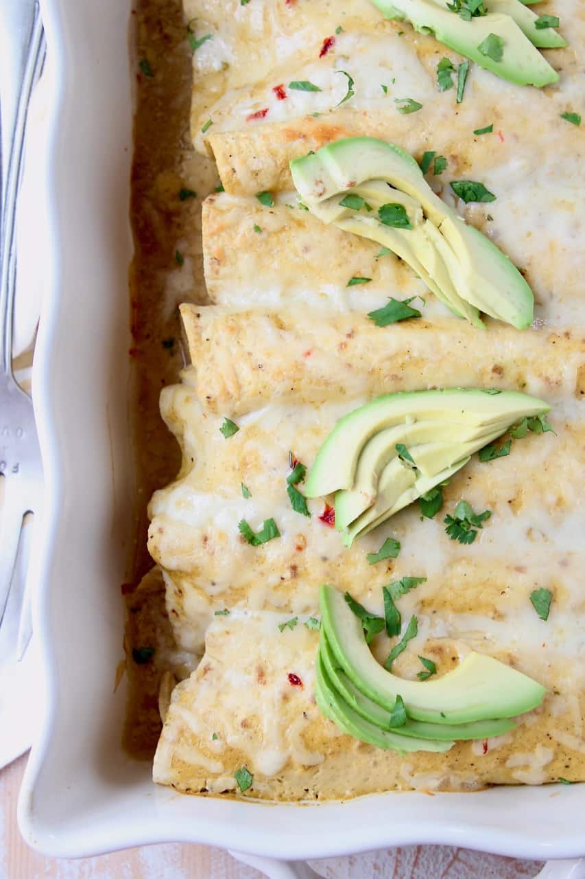 Enchiladas in casserole dish, topped with sliced avocado