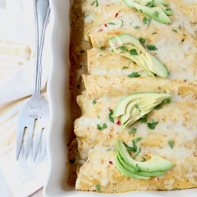 Overhead image of enchiladas with green sauce in casserole dish, topped with sliced avocado