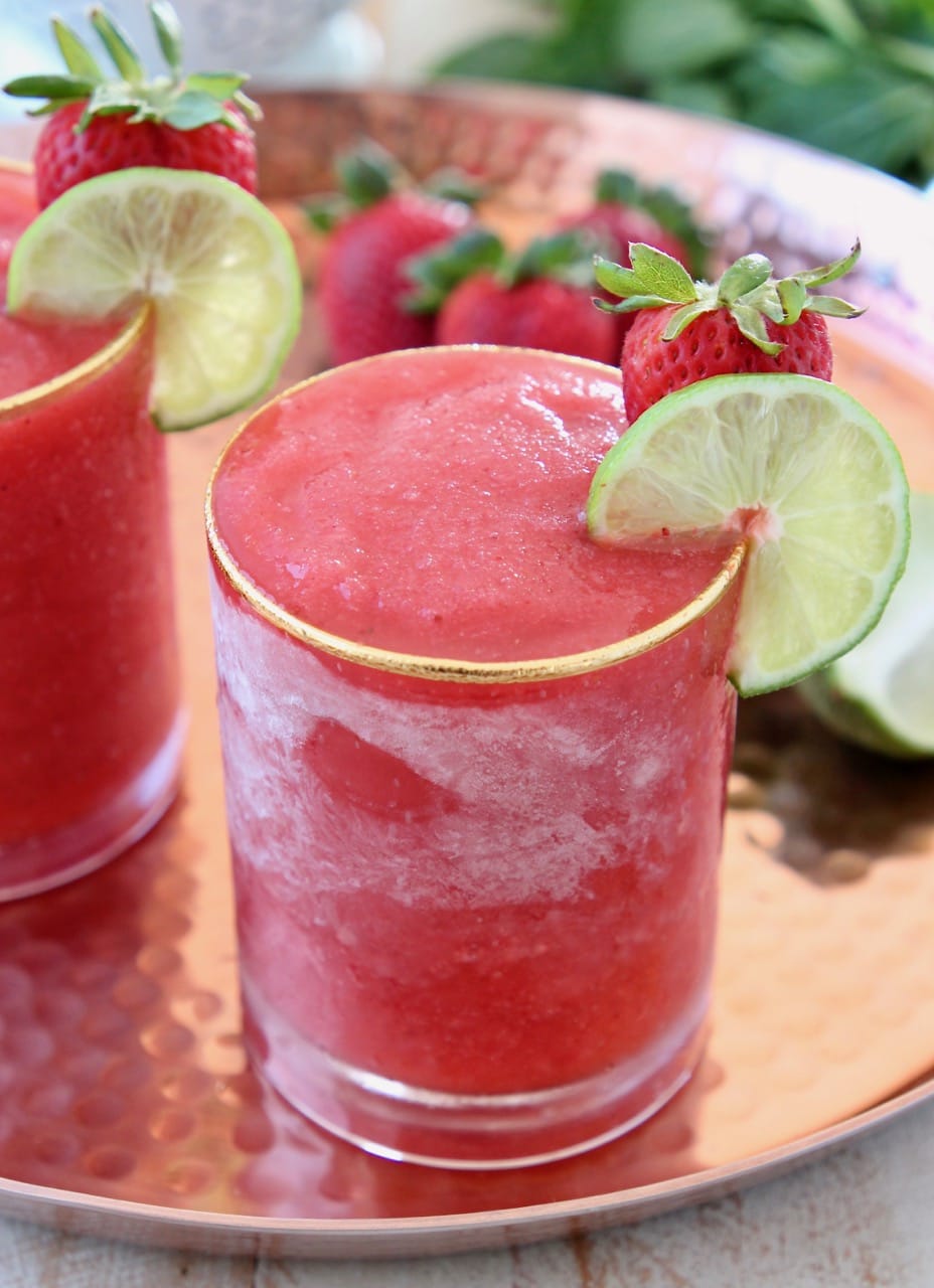 Frozen strawberry daiquiri in glass with lime wedge and strawberry on the side