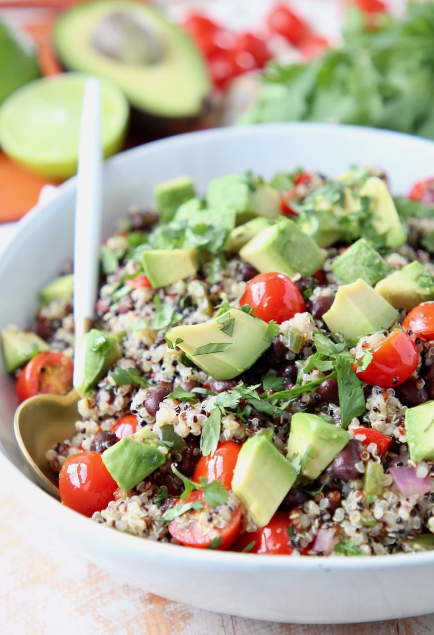 Mexican quinoa salad in bowl with white and gold spoon, topped with diced avocado