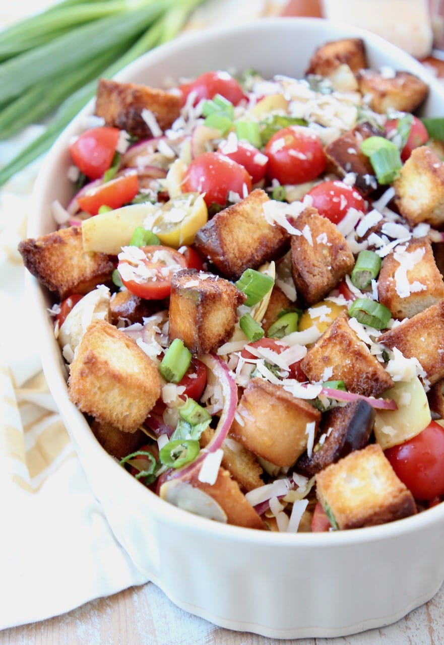 Panzanella salad in bowl with toasted bread pieces and halved cherry tomatoes, topped with grated parmesan cheese