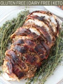 Sliced bacon wrapped turkey on plate with fresh herbs