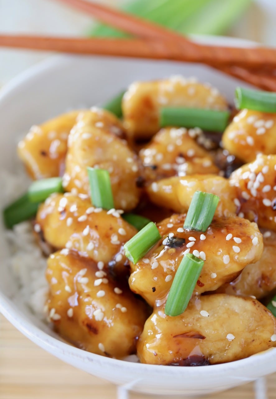 Chinese honey chicken pieces in bowl, topped with green onions and sesame seeds