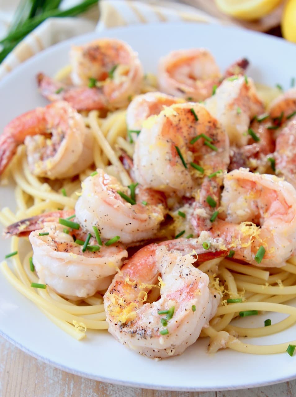Shrimp over pasta, topped with chives and lemon zest on white plate