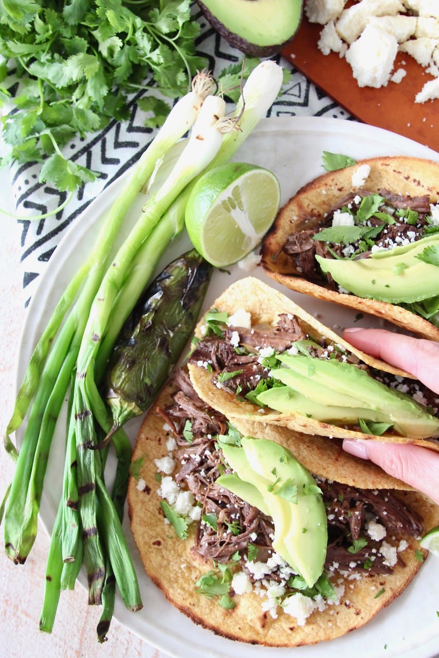 Slow Cooker Beef Barbacoa Tacos on Corn Tortillas with Sliced Avocado and Cotija Cheese