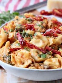 Vegetarian tortellini in white bowl with sun dried tomatoes, mushrooms and basil