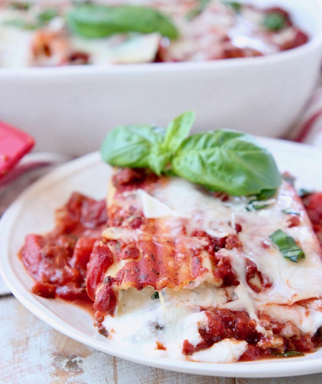 Cheese manicotti on plate, topped with marinara sauce and fresh basil leaves