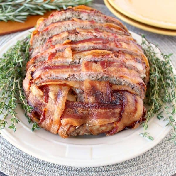 sliced meatloaf wrapped in bacon weave on plate with fresh thyme
