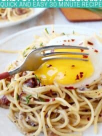 Fork cutting into egg yolk on top of pasta on plate