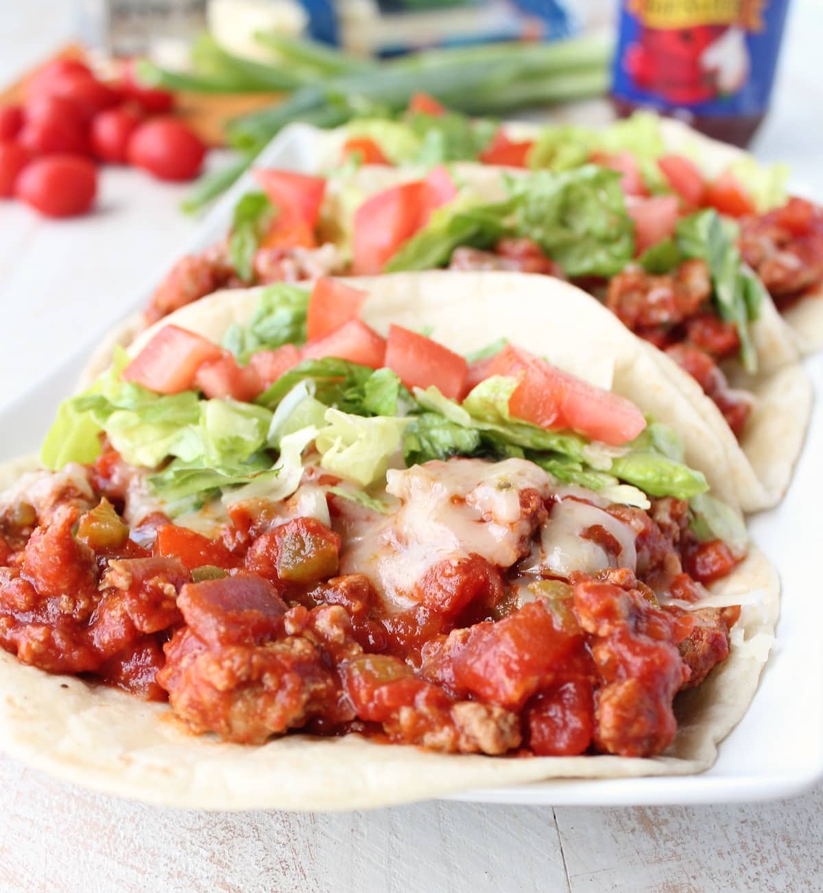 A flour tortilla filled with ground turkey in a red sauce topped with lettuce and tomatoes.
