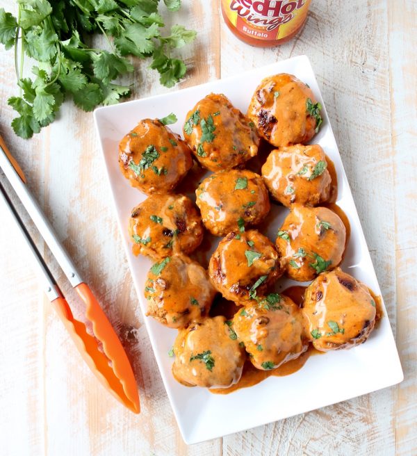 Honey Mustard Buffalo Meatballs on plate with orange tongs and fresh cilantro