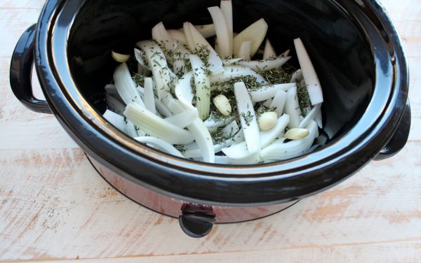 onion, garlic cloves and fresh rosemary in the bottom of a slow cooker. 