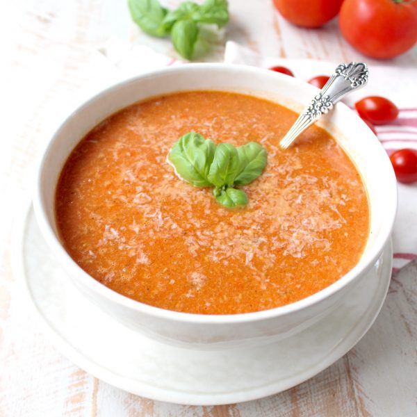tomato soup in bowl with spoon and basil leaves