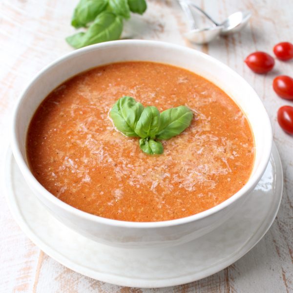 tomato soup in bowl topped with grated parmesan cheese and basil leaves