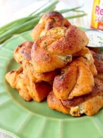 Mouth watering garlic knots are filled with cheese and smothered in buffalo sauce in this delicious recipe for cheesy garlic knots, perfect as an appetizer or party snack!