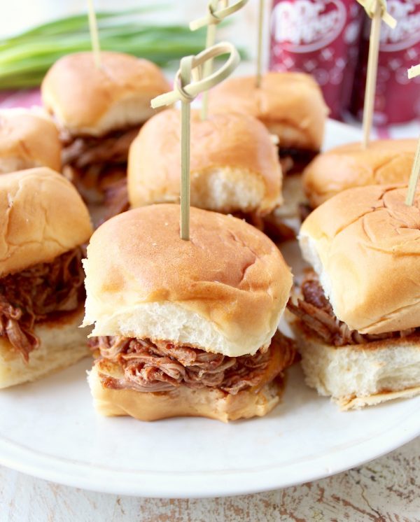 Hawaiian roll pulled pork sandwiches on a white plate with a toothpick in each one.