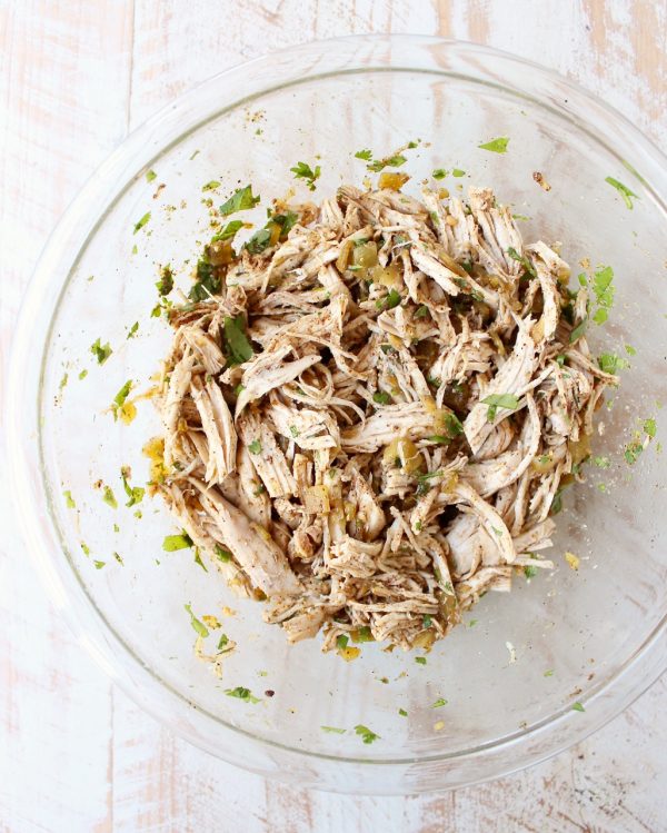 cooked shredded chicken tossed with green chilies and seasonings in glass bowl