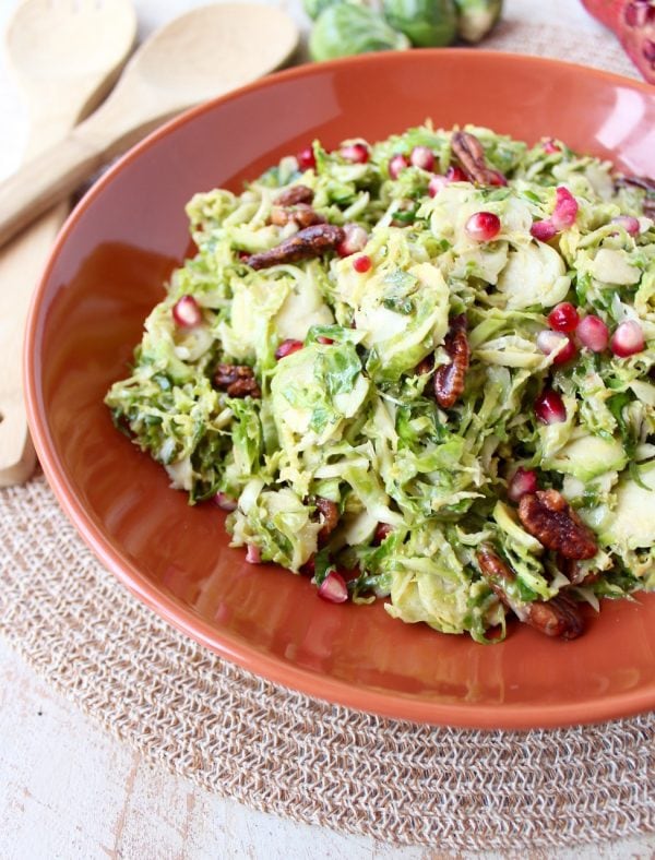 Serve this brussels sprout salad warm or cold as the perfect fall side dish! It's easy enough for weeknight dinners, but elegant enough for Thanksgiving dinner. This salad is tossed with a homemade dijon dressing, pomegranate seeds & pecans for a salad that's both colorful and flavorful!