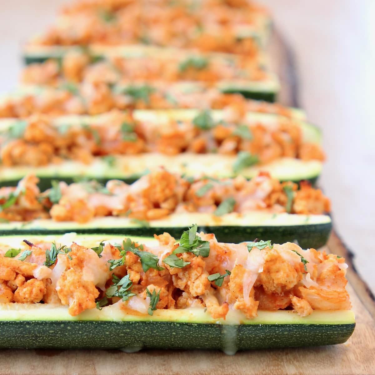 Buffalo Chicken Zucchini Boats with Pepper Jack Cheese and Cilantro on a wooden surface.