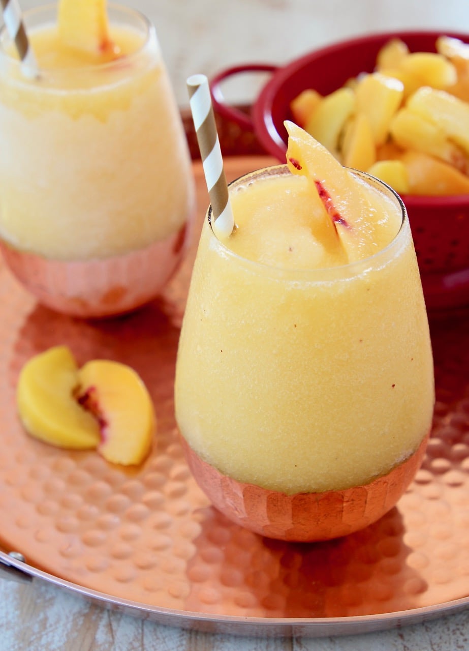 Frozen Peach Sangria with Fresh Peaches and Gold and White Striped Straw on Copper Tray