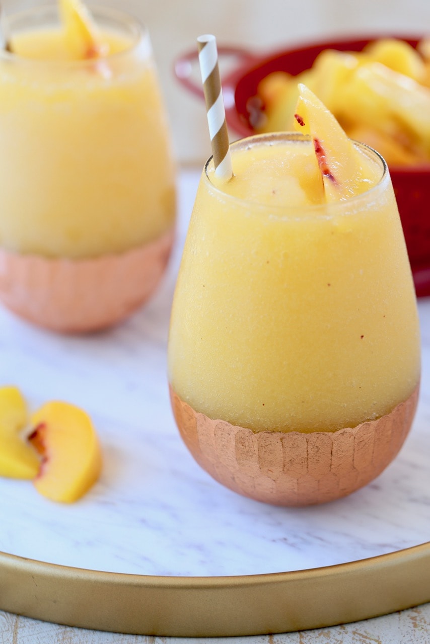 Frozen Peach Sangria in Copper Bottom Glasses on White Marble Serving Tray with Fresh Peaches