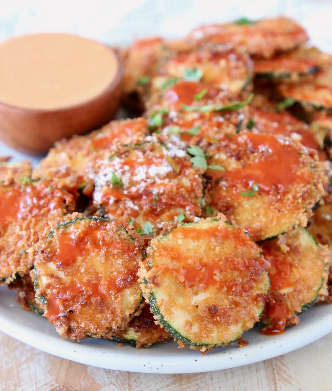Crispy zucchini chips on plate drizzled with buffalo sauce and parmesan cheese