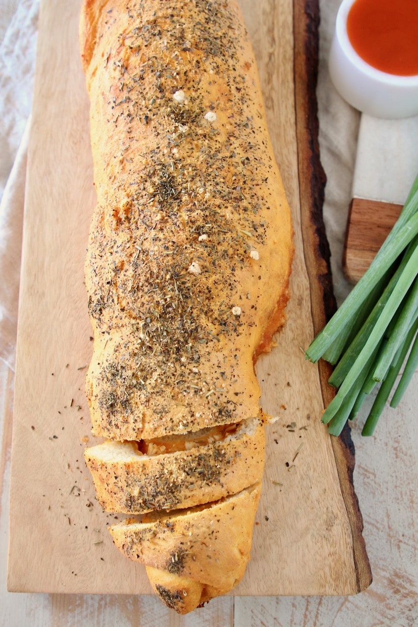 Buffalo cheesy pizza bread roll, sliced on wood cutting board with green onions